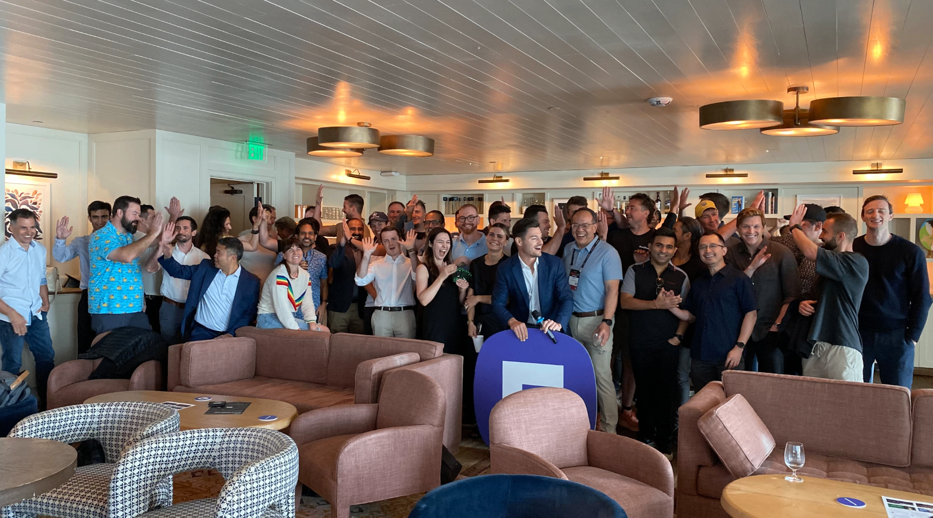 Large group of entrepreneurs and executives waving at mastermind event in luxurious lounge setting